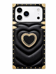 A black quilted leather phone case with gold-tone hardware, featuring a large heart design in the center and a decorative gold border around a smaller heart. The case has a white camera cutout at the top left and is shown on a plain white background.