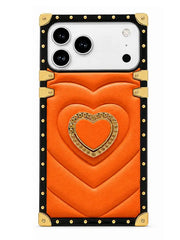 An orange phone case with a quilted chevron pattern, featuring a central gold heart design with rhinestone trim, a black border, and gold-tone metal corner protectors and rivets.