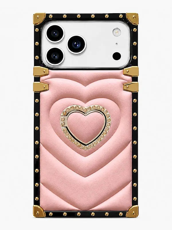 A pink quilted phone case with a central heart design, gold-tone studs, and a black border, shown on a white smartphone against a light gray background.