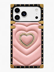 A pink quilted phone case with a central heart design, gold-tone studs, and a black border, shown on a white smartphone against a light gray background.