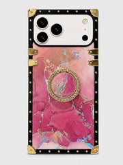 A protective phone case with a pink and magenta marble pattern, featuring a central gold-tone circular ring stand, a black border, and gold-tone rivets and corner protectors.