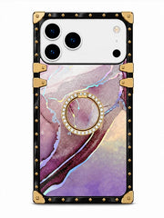 A protective phone case with a black frame featuring gold-tone rivets and corner protectors, a purple and pink marble pattern back, and an integrated circular ring stand embellished with small clear rhinestones.