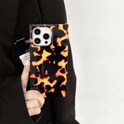 Phone case with tortoiseshell pattern held by a person wearing a black outfit.