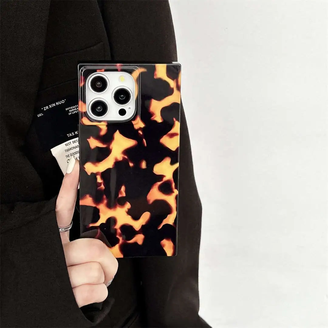 Phone case with tortoiseshell pattern held by a person wearing a black outfit.