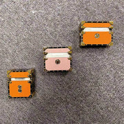 Three small Designer Style Earbud Protectors with gold accents on a gray surface