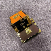 Two small Boutique AirPods accessories for women, one orange and one brown with gold accents, on a gray textured surface.