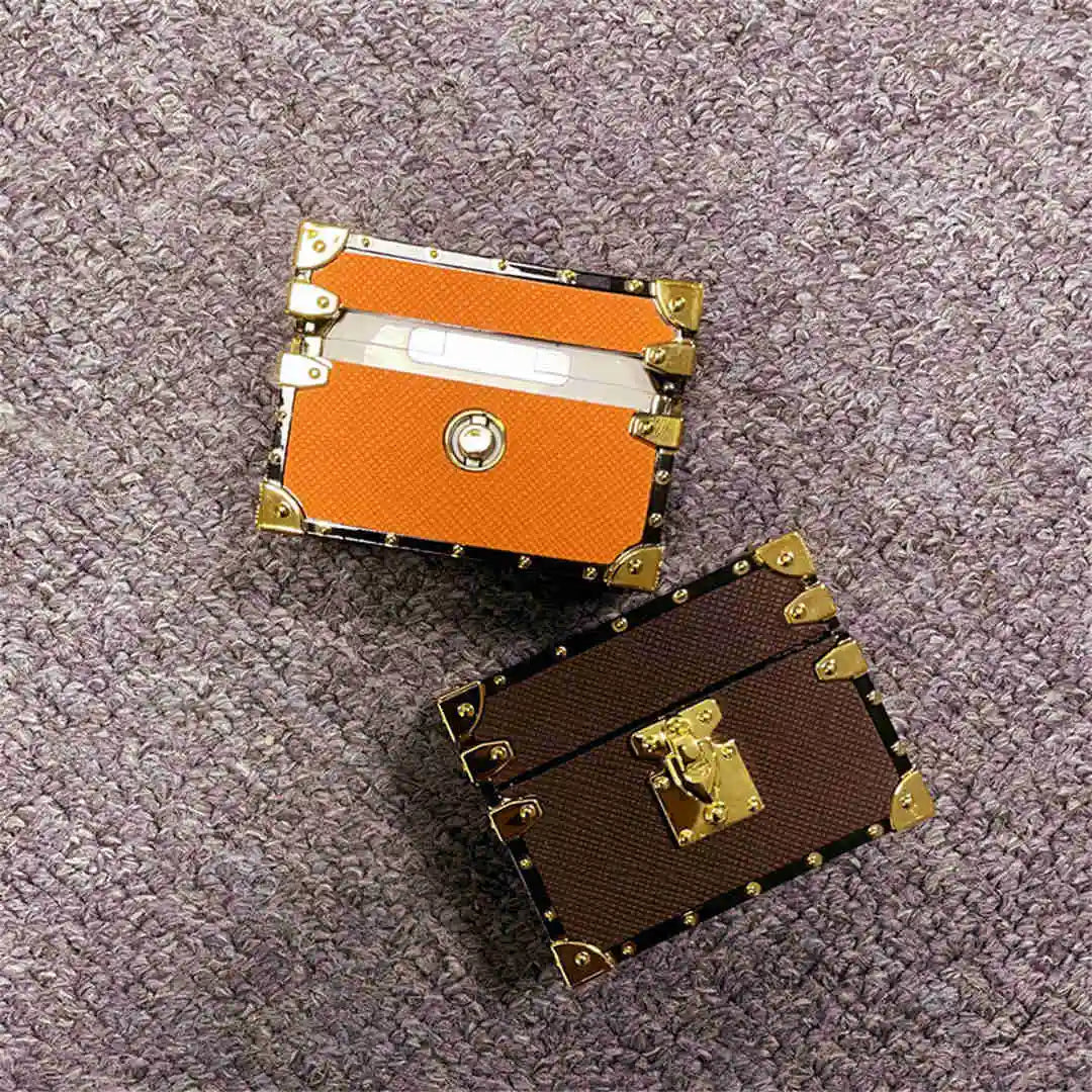 Two small decorative trunks AirPods cases, one orange and one brown, on a textured surface.