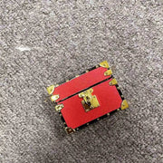 Red leather airpods case with gold accents on a gray surface