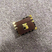 Small brown leather AirPods cover with gold accents on a gray textured surface