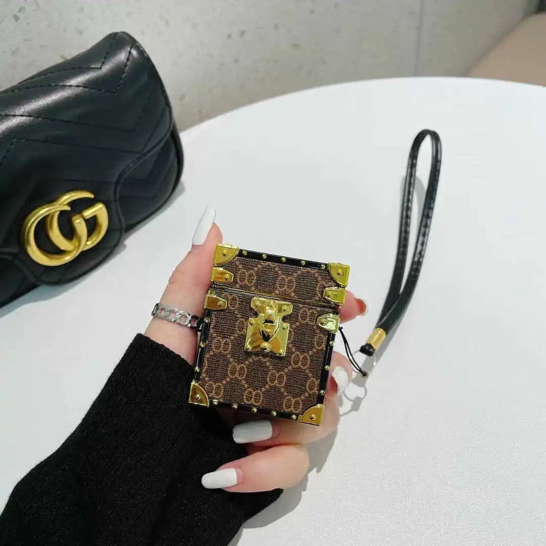 Hand holding a patterned AirPods trunk cover, next to a black handbag with a gold logo.