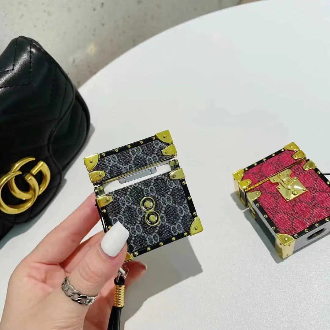 Hand holding a black and gold patterned AirPods trunk cover in the background on a white surface.