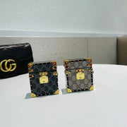 Two decorative AirPods trunk covers on a white surface next to a black handbag.