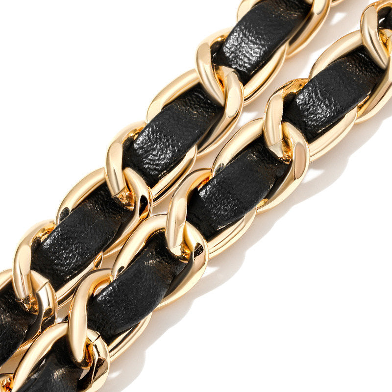 Gold chain bracelet with black leather links on a white background